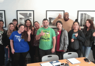 Career Placement Coordinator Ron Modesty and a group of graduates wave and give the camera a thumbs up.