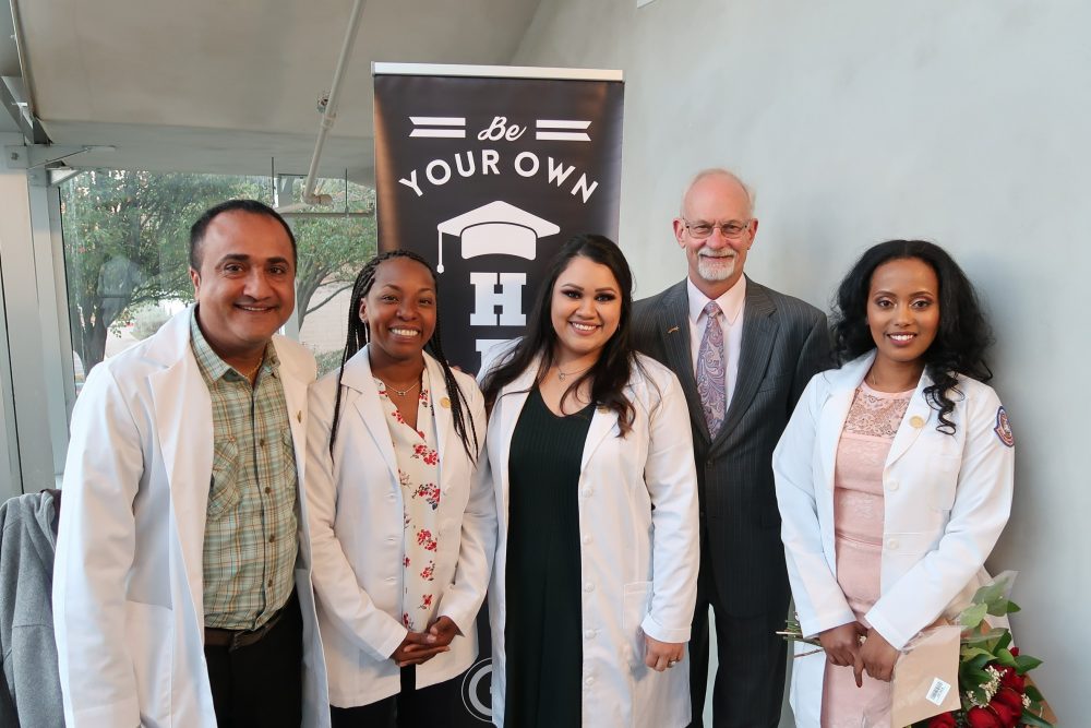 Nurse graduates together at their pinning ceremony standing in front of Capital IDEA's banner that reads: "Be Your Own Hero"